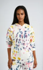 A young woman wearing a white tie die hoodie and trousers set with blue, yellow, purple and pink patterns