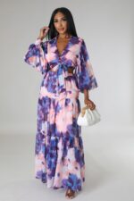 Woman in a floor length purple and pink maxi dress, against a grey background