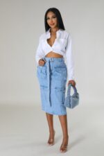 Woman against a neutral background, wearing a denim skirt and a white shirt