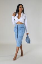 Woman against a neutral background, wearing a denim skirt and white shirt