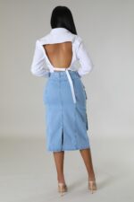 View from behind of a woman in a denim skirt and white top, with grey background
